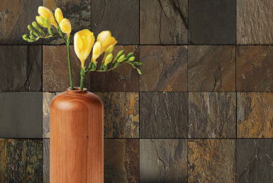 Kinara-distribución-y-venta-piedra-natural-30X30cm-interior-exterior-AQUA-GOLD pared de piedra natural tonos tierra florero naranja y flores amarillas