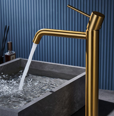 griferia-MONZA-ALTA-ORO-CEPILLADO Grifo dorado para baño, elegante y sofisticado, con lavamano gris y porcelanatos de fondo azul